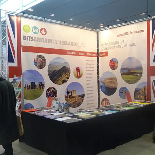 Messestand Bits - Rückwand mit Bildern von Orten in England im Kreisen und dem Union Jack an der Seite. Davor eine Auslage mit Prospekten.